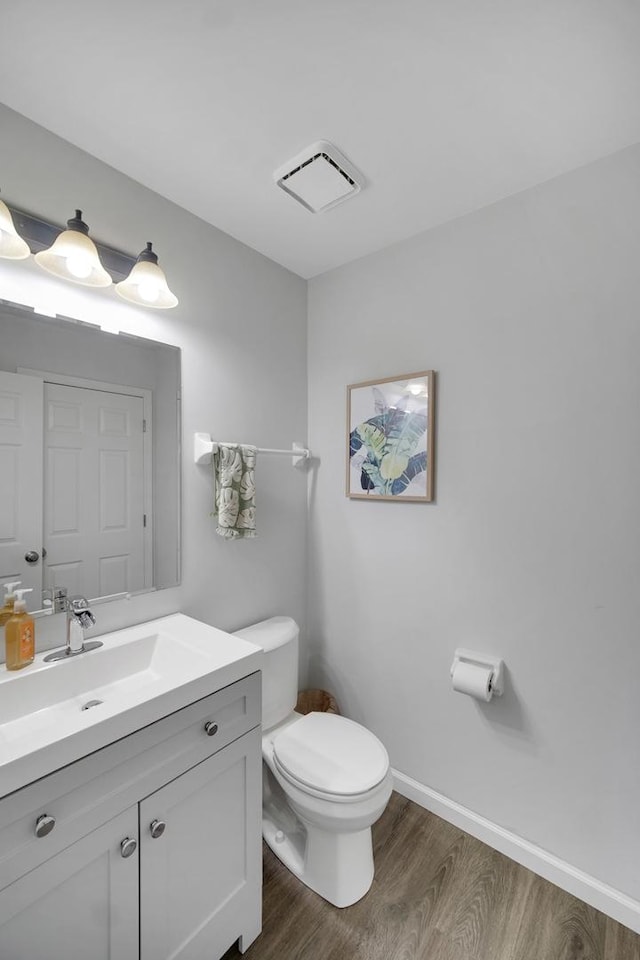 half bathroom with visible vents, wood finished floors, vanity, baseboards, and toilet