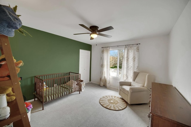 carpeted bedroom featuring a nursery area, ceiling fan, baseboards, and a closet