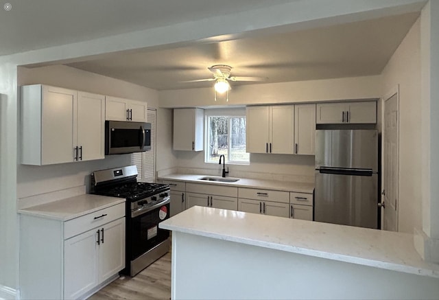 kitchen featuring a ceiling fan, appliances with stainless steel finishes, a sink, white cabinets, and light wood-style flooring