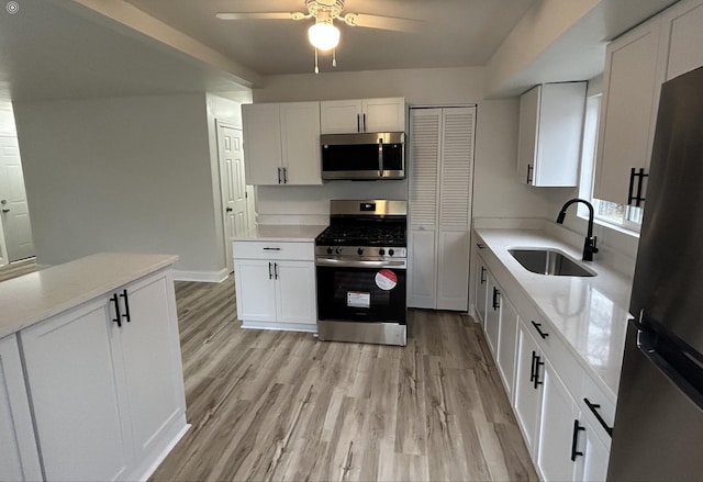 kitchen with ceiling fan, appliances with stainless steel finishes, a sink, white cabinets, and light wood finished floors