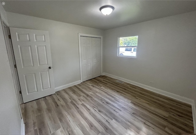 unfurnished bedroom featuring baseboards, a closet, wood finished floors, and visible vents
