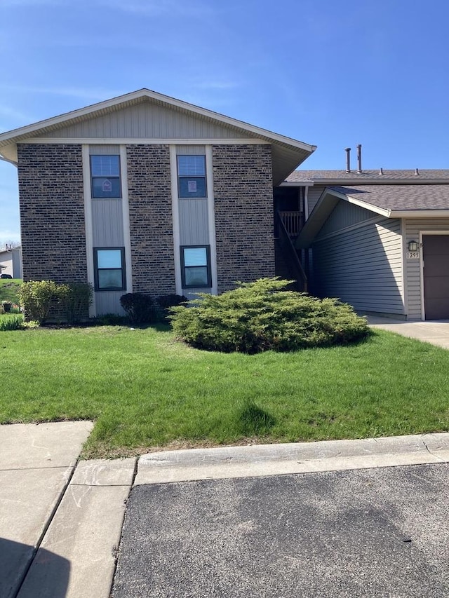 view of front of house featuring an attached garage, brick siding, and a front yard