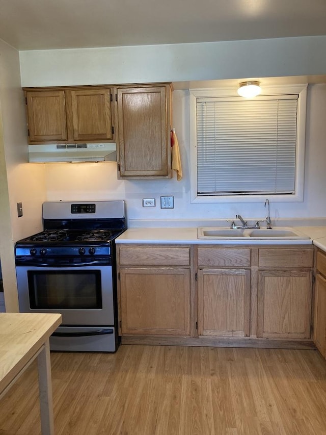 kitchen featuring stainless steel gas range oven, a sink, light countertops, under cabinet range hood, and light wood-style flooring