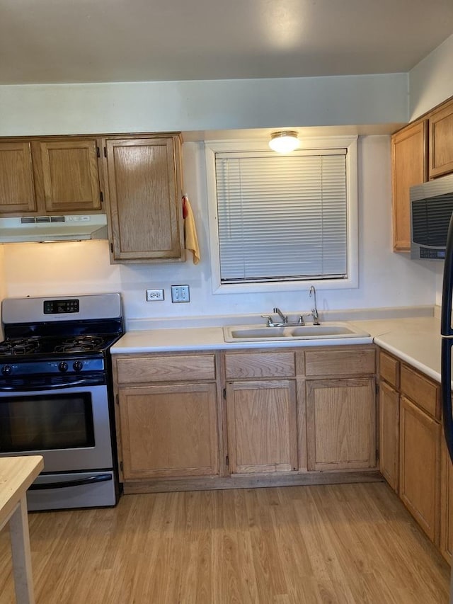 kitchen featuring a sink, light wood finished floors, light countertops, stainless steel appliances, and under cabinet range hood