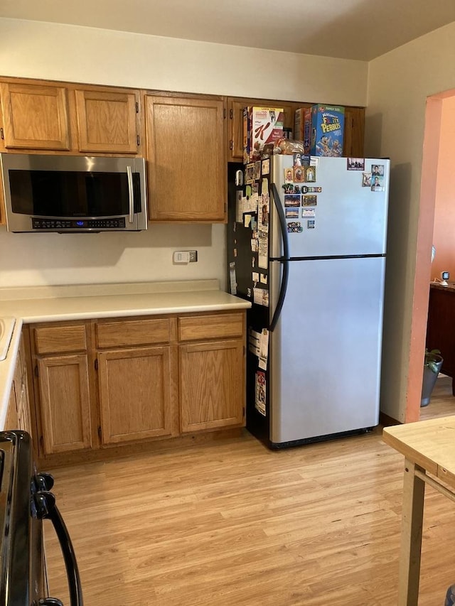 kitchen with freestanding refrigerator, light wood finished floors, stainless steel microwave, and light countertops