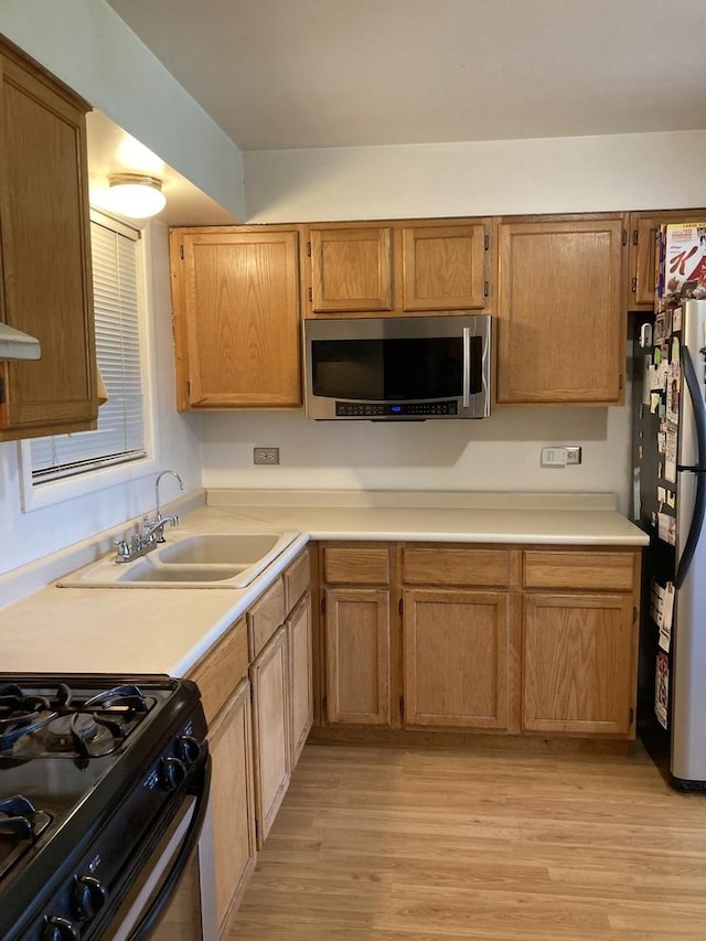 kitchen with light wood-style floors, light countertops, stainless steel appliances, and a sink
