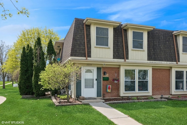 view of front facade with brick siding, a front lawn, and mansard roof