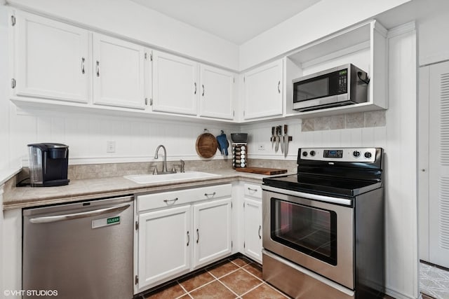 kitchen featuring dark tile patterned floors, a sink, light countertops, white cabinets, and stainless steel appliances