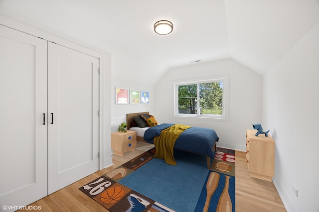 bedroom with light wood-style flooring, vaulted ceiling, and baseboards