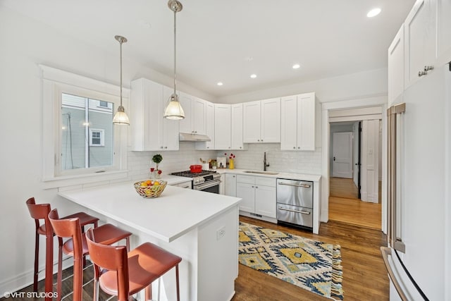 kitchen featuring premium appliances, under cabinet range hood, backsplash, a sink, and a peninsula