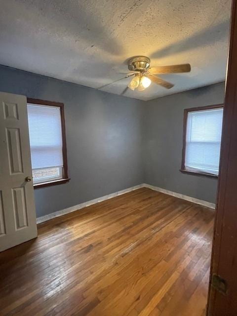 empty room with wood-type flooring, a textured ceiling, ceiling fan, and baseboards