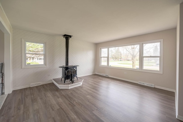 unfurnished living room featuring a wood stove, a wealth of natural light, baseboards, and visible vents