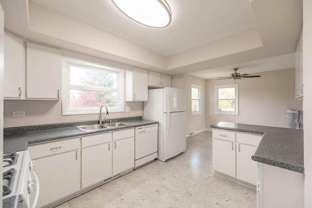 kitchen with dark countertops, a raised ceiling, a sink, and white appliances