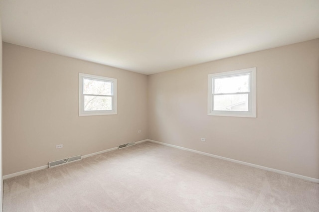 unfurnished room with a wealth of natural light, visible vents, and light colored carpet