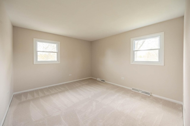 spare room with baseboards, light carpet, and visible vents