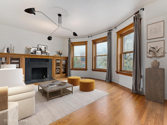 living room with baseboards, a brick fireplace, and light wood-type flooring