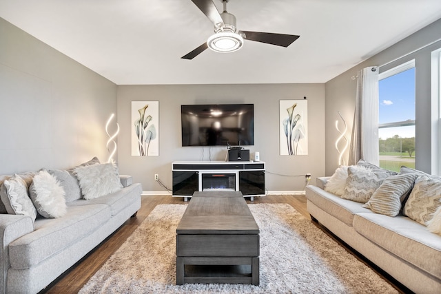 living room featuring a ceiling fan, baseboards, and wood finished floors