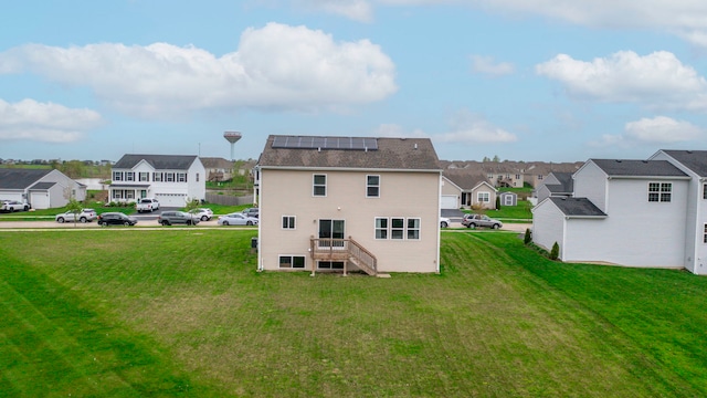 back of property featuring a yard, a residential view, and solar panels
