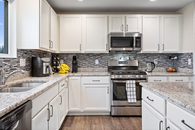 kitchen with white cabinets, appliances with stainless steel finishes, a sink, dark wood finished floors, and decorative backsplash