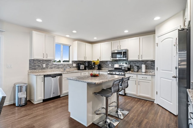 kitchen with white cabinets, dark wood-style flooring, a sink, stainless steel appliances, and tasteful backsplash