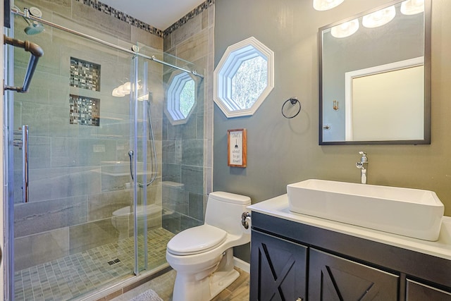 bathroom with a stall shower, toilet, vanity, and wood finished floors
