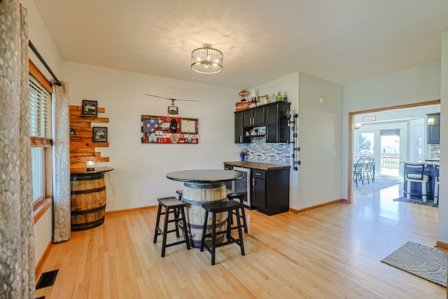 dining area with light wood-type flooring, a chandelier, bar, and baseboards