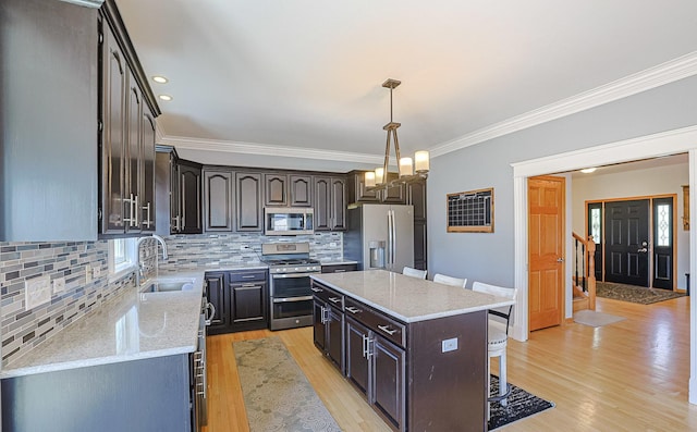 kitchen featuring stainless steel appliances, a sink, a kitchen breakfast bar, a center island, and crown molding