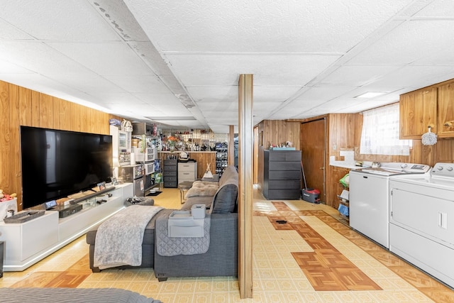 basement with light floors, a paneled ceiling, wooden walls, and washing machine and clothes dryer