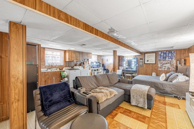 living area with wooden walls, visible vents, washing machine and clothes dryer, and a paneled ceiling