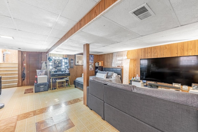 living room featuring visible vents, wooden walls, stairway, a paneled ceiling, and tile patterned floors