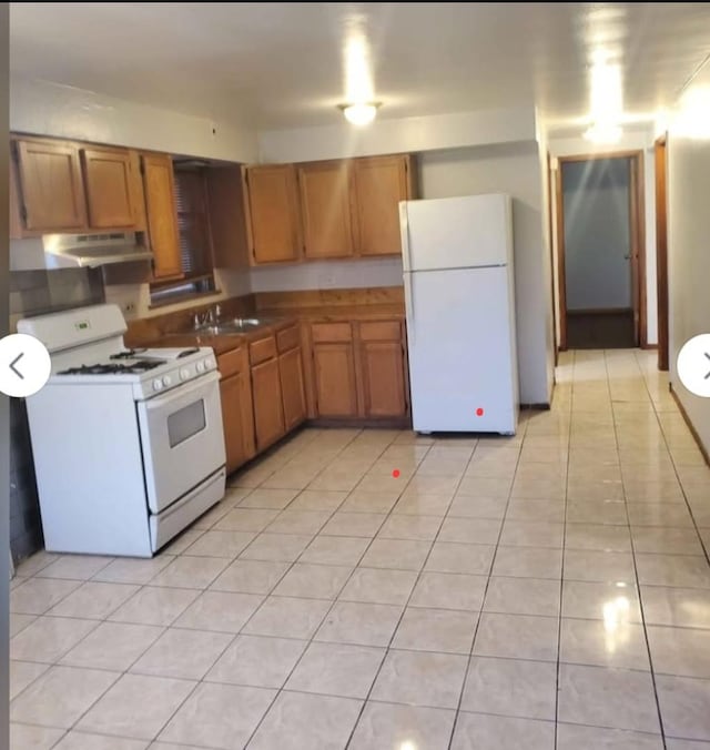 kitchen with white appliances, under cabinet range hood, light tile patterned floors, and brown cabinets