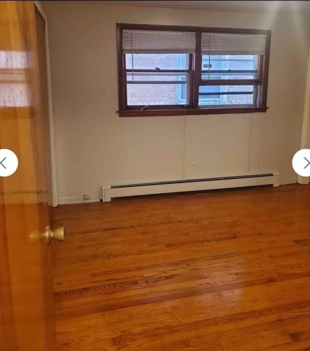 empty room featuring wood finished floors and a baseboard radiator