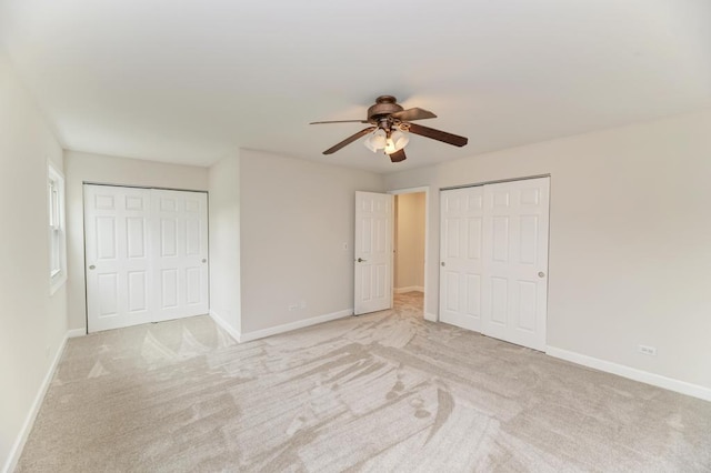 unfurnished bedroom featuring baseboards, multiple closets, light carpet, and ceiling fan