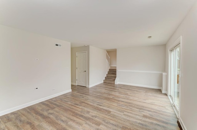 spare room with light wood-style floors, stairs, baseboards, and visible vents