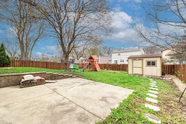 view of yard with a storage unit, a fenced backyard, an outbuilding, a playground, and a patio