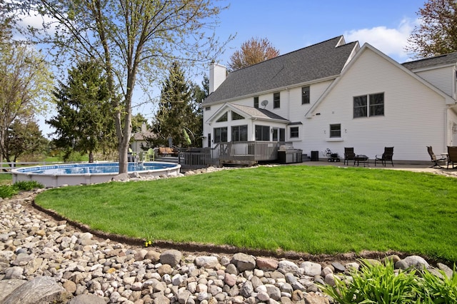 back of house featuring an outdoor pool, a wooden deck, a yard, and a chimney