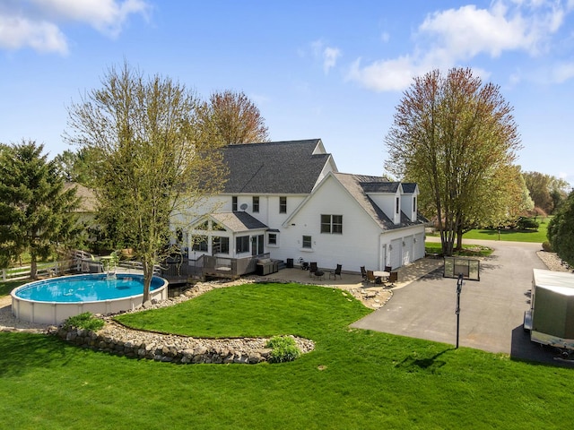 rear view of house featuring a garage, a wooden deck, an outdoor pool, a patio area, and a lawn