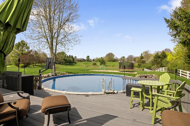 outdoor pool with fence, a trampoline, a yard, and a deck