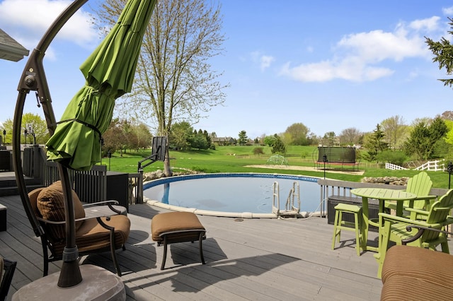 pool featuring a lawn, a wooden deck, and a trampoline
