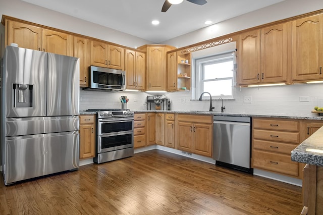 kitchen with appliances with stainless steel finishes, tasteful backsplash, light stone countertops, a sink, and recessed lighting
