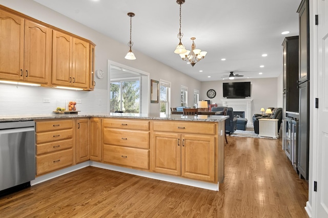 kitchen featuring a peninsula, wood finished floors, a fireplace, ceiling fan with notable chandelier, and dishwasher