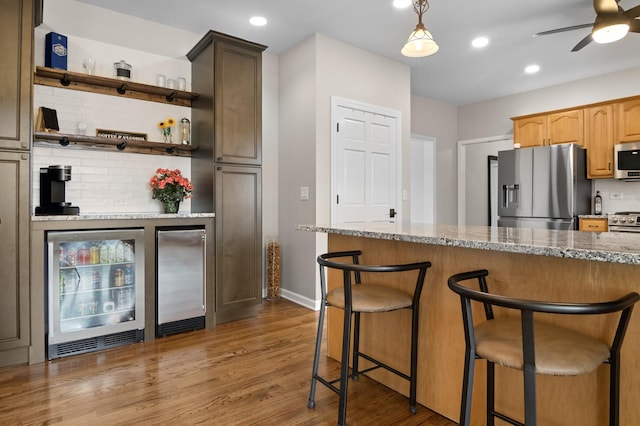 interior space featuring appliances with stainless steel finishes, a breakfast bar area, beverage cooler, and wood finished floors