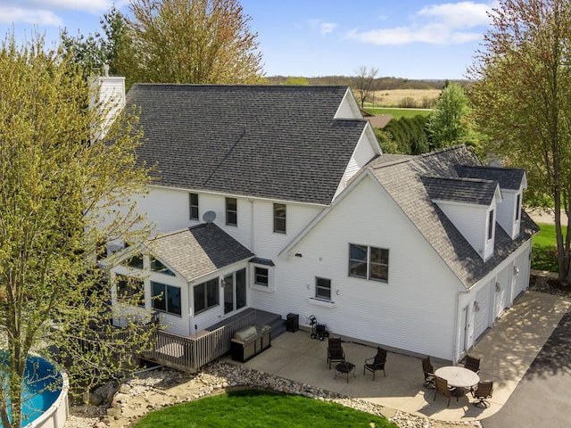 back of house with a chimney, a deck, a patio area, an attached garage, and a shingled roof