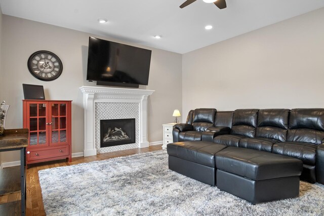 living area featuring a tiled fireplace, baseboards, ceiling fan, and wood finished floors