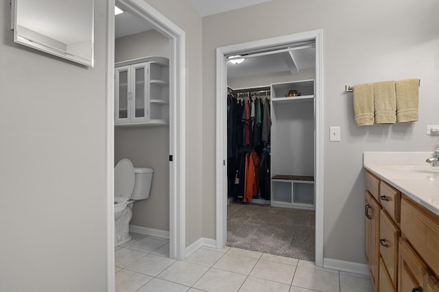 bathroom featuring vanity, toilet, tile patterned floors, baseboards, and a spacious closet