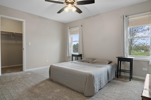 bedroom with a walk in closet, baseboards, carpet, and ceiling fan