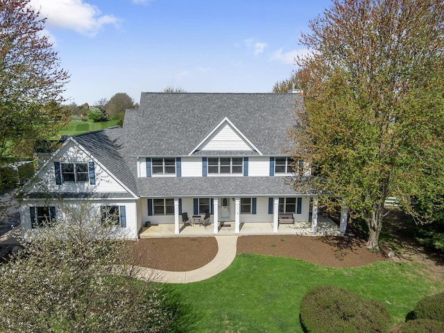 view of front of house featuring covered porch, a shingled roof, and a front lawn
