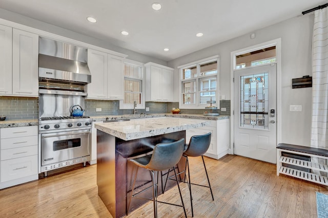 1800 W Melrose St, Chicago, IL 60657 - kitchen featuring wall chimney range hood, premium stove, a breakfast bar, backsplash, and white cabinetry