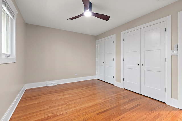 unfurnished bedroom featuring ceiling fan, light wood finished floors, multiple closets, baseboards, and visible vents