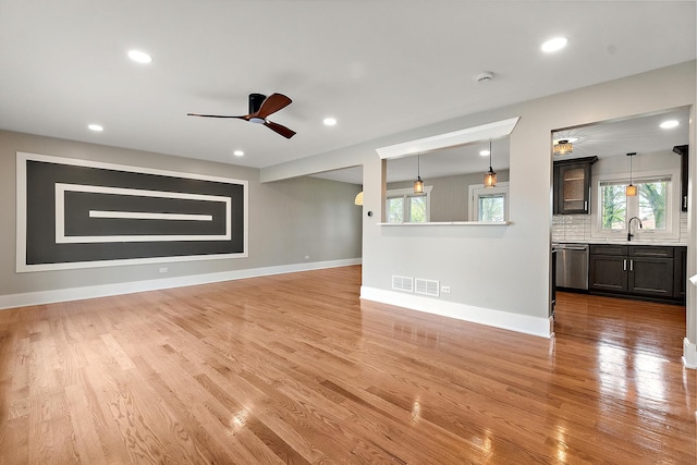 unfurnished living room with a sink, plenty of natural light, a ceiling fan, baseboards, and light wood-type flooring